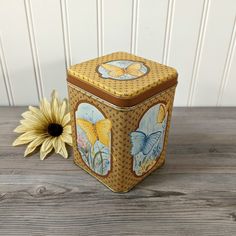 a yellow and brown box sitting on top of a wooden table next to a flower