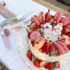 a cake with strawberries and macaroni on it sitting on a table next to a knife