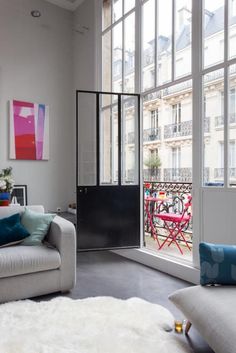 a living room filled with furniture next to large windows and white rugs on the floor