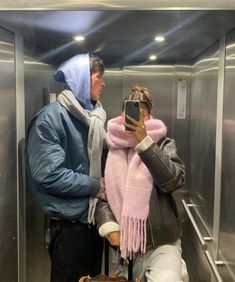 a man and woman standing in an elevator looking at their cell phones