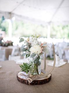 a vase filled with white flowers sitting on top of a wooden table under a tent