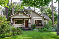 a small house in the middle of some trees and grass with flowers on it's front lawn