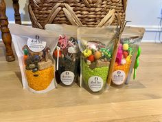 three bags of food sitting on top of a wooden table next to a basket filled with carrots