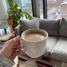 a person holding a cup of coffee in front of a couch with a large window