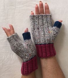 two hands wearing knitted mittens on top of a white sheet with one hand in the air