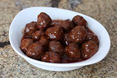 a white bowl filled with meatballs covered in ketchup on top of a counter