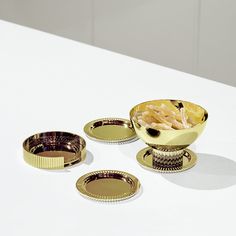 three gold dishes on a white table, one has fries in it and the other is empty