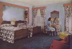 a woman sitting at a desk in a room with two beds and curtains on the windows