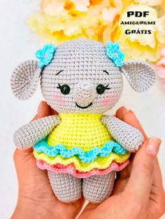 a small crocheted stuffed animal in a yellow and blue dress with flowers behind it