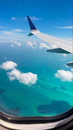 the wing of an airplane flying over blue water and clouds in the sky, seen from above