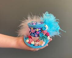 a hand holding a colorful hat with flowers and feathers on it's top,