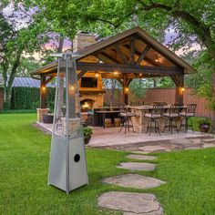 an outdoor kitchen and grill in the middle of a yard with grass, trees, and stepping stones