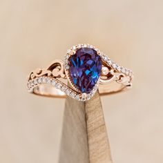 a tan gold ring with an oval blue stone and diamond accents on the band, sitting on top of a piece of wood