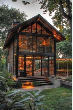 a small house with lots of windows and steps leading up to the front door, surrounded by greenery