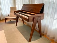 a wooden piano sitting on top of a rug in front of a curtained window