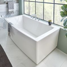 a large white bath tub sitting in a bathroom next to a window with lots of greenery