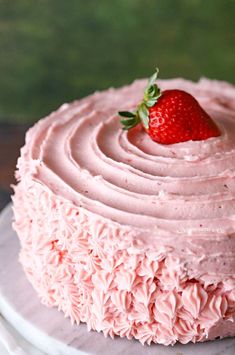 a cake with pink frosting and a strawberry on top is sitting on a plate