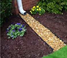 a garden path made out of rocks and gravel in front of a brick wall with flowers