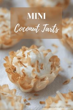 mini coconut tarts with white frosting and toasted coconut on top, sitting on a paper towel