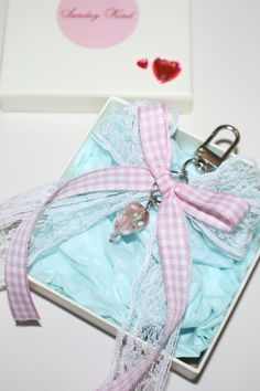 a pink and white ribbon tied around a keychain in a box with a heart on it