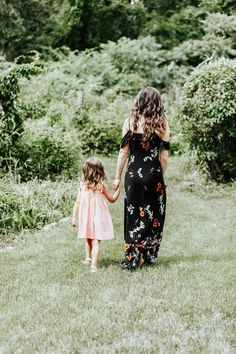 a mother and her daughter walking through the grass in front of some bushes holding hands