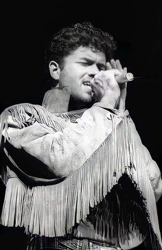 a man holding a microphone in his right hand and wearing a jacket with fringes on it