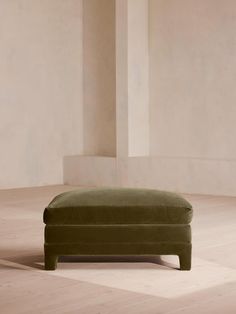 a green ottoman sitting on top of a hard wood floor next to a white wall