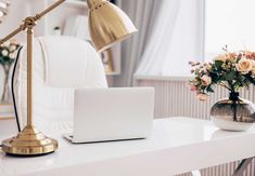 a laptop computer sitting on top of a white desk next to a vase with flowers