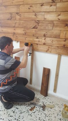 a man in grey shirt and black pants working on wood paneling with an electric drill