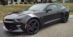 a black chevrolet camaro is parked in front of a house