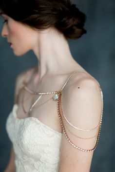 a woman in a white dress wearing a gold chain and pearled necklace on her shoulder