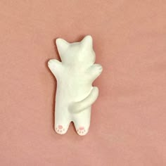 a white cat figurine laying on top of a pink surface