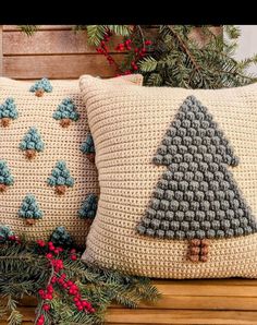 two crocheted christmas pillows on a bench with pine cones and evergreen branches in the background