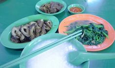 a green table topped with plates filled with food and chopsticks on top of it