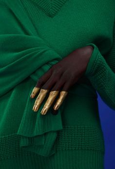 a woman's hand with gold painted nails and green sweater, holding her hands on her hip