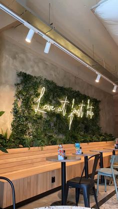 the inside of a restaurant with wooden benches and green plants on the wall behind it