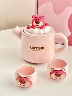 a pink tea pot with two cups and a teddy bear on top, next to it