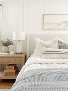 a bed with white sheets and pillows in a bedroom next to a wooden table topped with two lamps