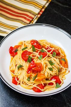 a plate of spaghetti with tomatoes and basil on top, sitting on a table next to a napkin