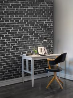 a desk and chair in front of a brick wall with a framed photograph on it