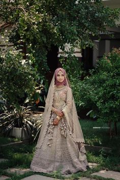 a woman in a wedding dress standing on the grass with trees and bushes behind her