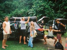 a group of people standing in front of a car with their arms up and holding tennis rackets