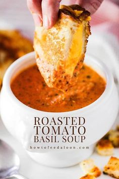 a person dipping food into a bowl of tomato basil soup with bread croutons on the side