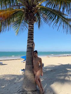 a woman leaning up against a palm tree on the beach