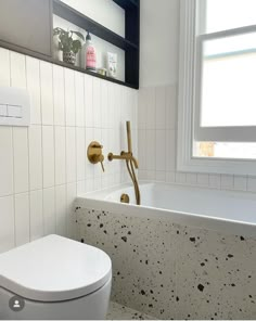 a white toilet sitting next to a bath tub in a bathroom under a windowsill