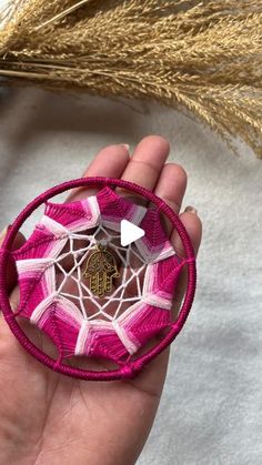 a hand holding a pink and white ornament on top of a piece of string