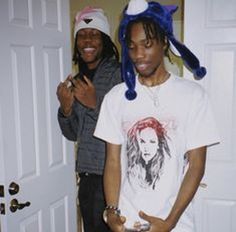 two young men standing next to each other in front of a door with one holding a cell phone