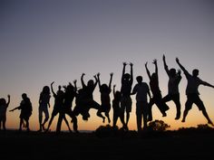 a group of people jumping in the air at sunset