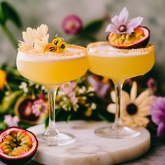 two glasses filled with drinks sitting on top of a marble table next to some flowers