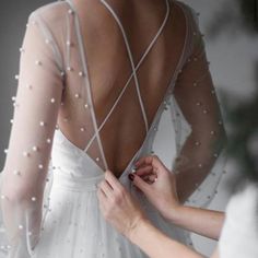 the back of a woman's wedding dress with pearls on it, being fitted